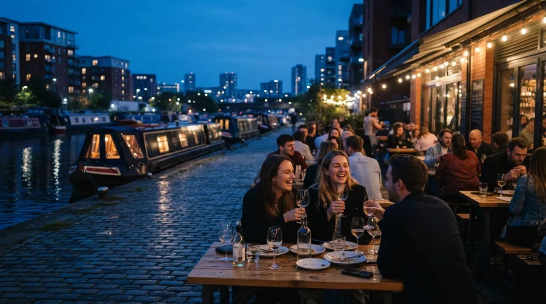 die Terrasse von Flawd am New Islington Marina zur blauen Stunde, Weingläser auf Tischen und Kanalboote vertäut am Wasser