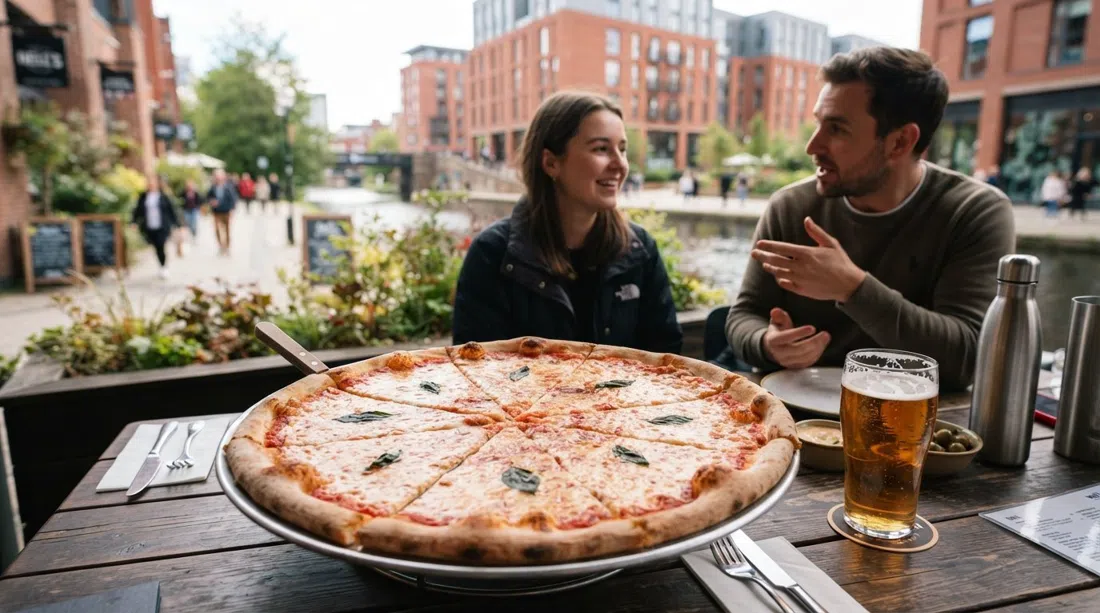una pizza gigante al estilo de Nueva York en Nell's en Kampus, con una cerveza artesanal en la mesa y el jardín junto al canal borroso al fondo